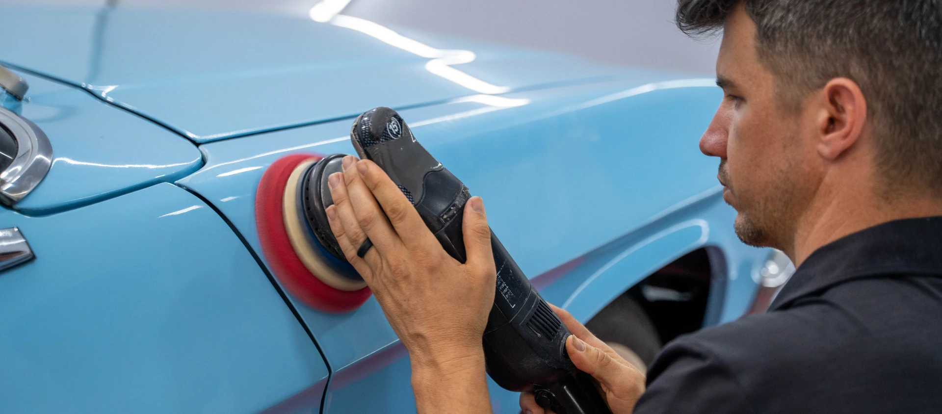 Detailer machine polishing a light blue classic car during a paint correction